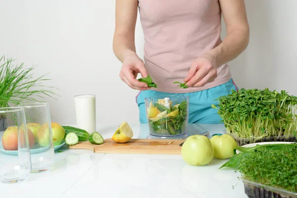 step-by-step recipe for making smoothies from micro-green apples cucumber and spinach. woman hands cut vegetables and put them in blender for whipping eco organic fresh food detox on light background.