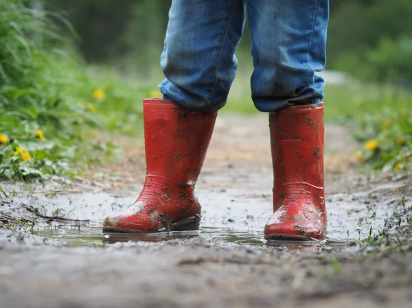 child\'s feet in the muddy, wet jeans and rubber boots
