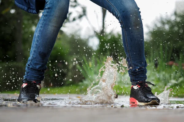 Human Legs in jeans and sneakers in a puddle. Splashes of water. Run, jump in puddles