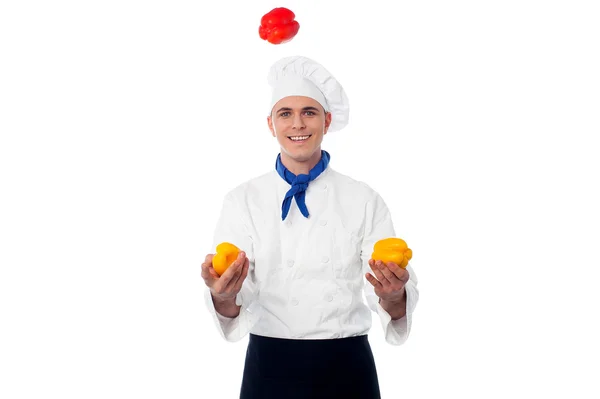 Jeune chef jonglant avec des poivrons — Photo