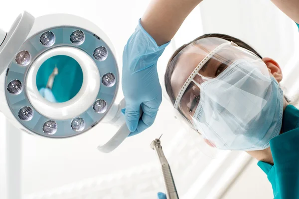 Dentista feminino ajustando lâmpada dentária — Fotografia de Stock