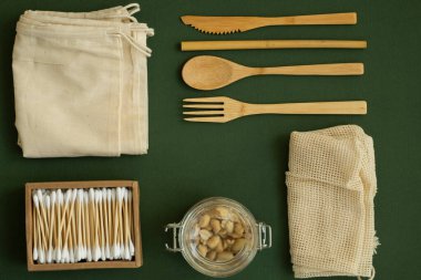 Sıfır atık. Çevre dostu bambu çatal bıçak takımı, ağ pamuk torbaları, fındıklı cam kavanozlar ve bir kutu pamuklu çubuk. Plastiksiz konsept. Yeşil yüzeyde doğal ve yeniden kullanılabilir ögeler aksesuarlar.