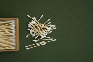 Çevre dostu pamuklu çubuklar. Yeşil bir yüzey üzerinde geri dönüşümlü bambu tomurcukları içeren karton bir kutu. Sıfır atık. Eko ürün. Kozmetik çubuklar kutuda. Kulakları temizlemek için tahta sopalar..