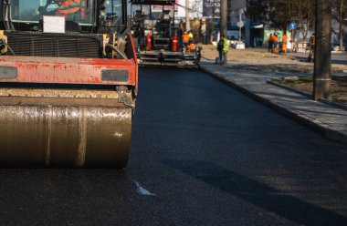 Ağır titreşimli paten sıkıştırıcılı asfalt yol silindiri bir yol inşaatındaki yolda yeni bir sıcak asfalta bastırıyor. Asfalt kaldırımda ağır titreşimli silindir çalışıyor. Onarılıyor.
