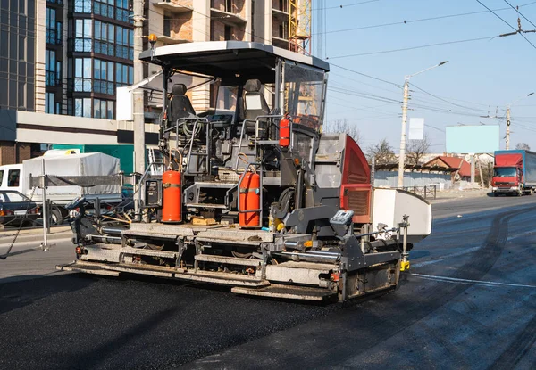 Industrial asphalt paver machine laying fresh asphalt on road construction site on the street. A Paver finisher placing a layer of a new hot asphalt on the roadway on a construction site. Repairing.