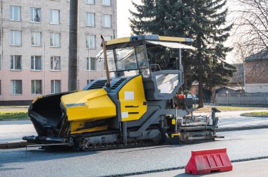 Endüstriyel asfalt kaldırım makinesi sokaktaki yol şantiyesine taze asfalt seriyor. Bir Paver bitirici, inşaat alanındaki yola yeni bir asfalt tabakası yerleştiriyor. Onarılıyor.
