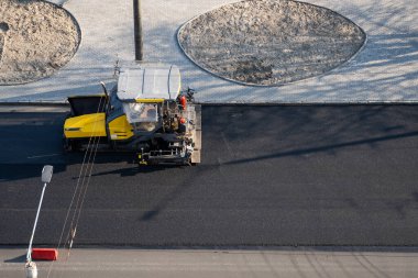 Endüstriyel asfalt kaldırım makinesi sokaktaki yol şantiyesine taze asfalt seriyor. Bir Paver bitirici, inşaat alanındaki yola yeni bir asfalt tabakası yerleştiriyor. Onarılıyor.