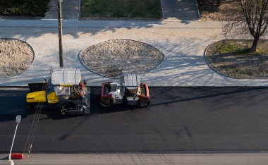 Taze asfalt döşeyen endüstriyel asfalt kaldırım makinesi ve titreşim silindirli ağır bir yol silindiri bir yol inşaatı alanında yeni bir sıcak asfalta bastırıyor..