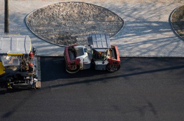 Taze asfalt döşeyen endüstriyel asfalt kaldırım makinesi ve titreşim silindirli ağır bir yol silindiri bir yol inşaatı alanında yeni bir sıcak asfalta bastırıyor..