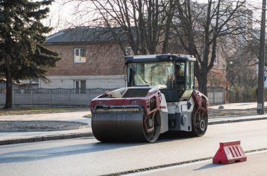 Ağır titreşimli paten sıkıştırıcılı asfalt yol silindiri bir yol inşaatındaki yolda yeni bir sıcak asfalta bastırıyor. Asfalt kaldırımda ağır titreşimli silindir çalışıyor. Onarılıyor.