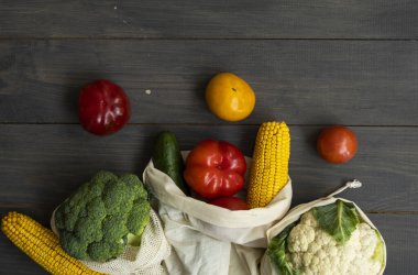 Sıfır atık. Biber, domates, mısır, salatalık, brokoli, tekrar kullanılabilir alışveriş ekosu dostu pamuk torbalarda karnabahar. Tahta bir masada sebzeler eko torbanın içinde. Plastiksiz konsept.