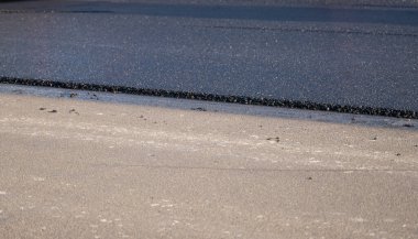 Yeni bırakılmış siyah ziftsiz asfalt, yapıyı gösteren çakılların kenarları yüksek. Yollara yeni bir asfalt seriyorum. Yolun inşaatı.