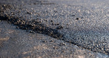 Yeni bırakılmış siyah ziftsiz asfalt, yapıyı gösteren çakılların kenarları yüksek. Yollara yeni bir asfalt seriyorum. Yolun inşaatı.