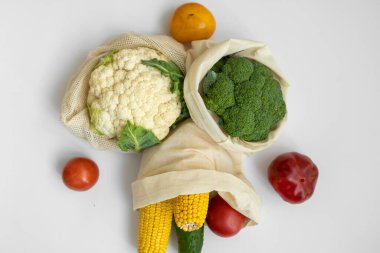 Beyaz yüzeyde sebzeler eko torbanın içinde. Biber, domates, mısır, salatalık, brokoli, tekrar kullanılabilir alışveriş ekosu dostu pamuk torbalarda karnabahar. Sıfır atık ve plastiksiz konsept. Sürdürülebilir.