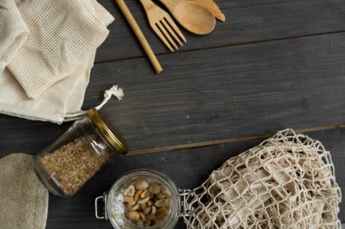 Sıfır atık. Çevre dostu bambu çatal bıçak takımı ve temizlik fırçaları, ağ pamuk torbaları, cam kavanozlar, lif ve bambu diş fırçaları. Ahşap yüzeydeki doğal ve yeniden kullanılabilir eşyalar.