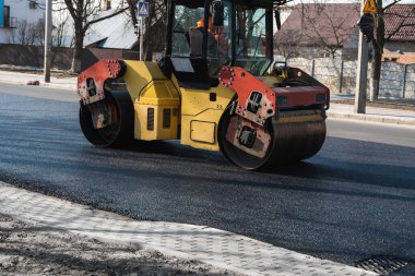 Ağır titreşimli paten sıkıştırıcılı asfalt yol silindiri bir yol inşaatındaki yolda yeni bir sıcak asfalta bastırıyor. Asfalt kaldırımda ağır titreşimli silindir çalışıyor. Onarılıyor.