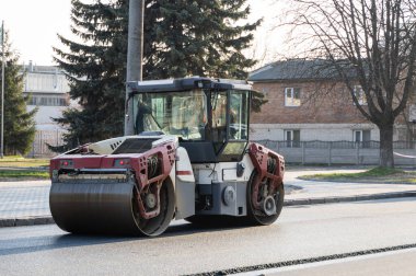 Ağır titreşimli paten sıkıştırıcılı asfalt yol silindiri bir yol inşaatındaki yolda yeni bir sıcak asfalta bastırıyor. Asfalt kaldırımda ağır titreşimli silindir çalışıyor. Onarılıyor.
