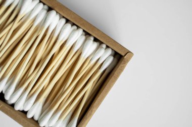 Çevre dostu pamuklu çubuklar. Gri bir yüzey üzerinde geri dönüşümlü bambu tomurcukları içeren karton bir kutu. Sıfır atık. Eko ürün. Kozmetik çubuklar kutuda. Kulakları temizlemek için tahta sopalar..