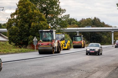 KYIV, UKRAINE - 25 Eylül 2020: İki ağır asfalt yol silindiri ve ağır titreşimli paten sıkıştırıcısı bir cadde üzerindeki yol inşaatında yeni bir sıcak asfalta baskı yapıyor..