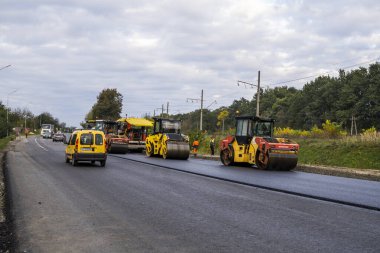 KYIV, UKRAINE - 25 Eylül 2020: İki ağır asfalt yol silindiri ve ağır titreşimli paten sıkıştırıcısı bir cadde üzerindeki yol inşaatında yeni bir sıcak asfalta baskı yapıyor..