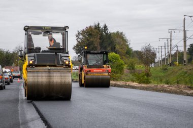KYIV, UKRAINE - 25 Eylül 2020: İki ağır asfalt yol silindiri ve ağır titreşimli paten sıkıştırıcısı bir cadde üzerindeki yol inşaatında yeni bir sıcak asfalta baskı yapıyor..