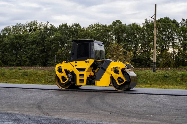 Asphalt road roller with heavy vibration roller compactor press new hot asphalt on the roadway on a road construction site. Heavy Vibration roller at asphalt pavement working. Repairing.