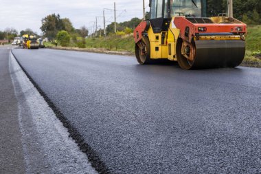 Ağır titreşimli paten sıkıştırıcılı asfalt yol silindiri bir yol inşaatındaki yolda yeni bir sıcak asfalta bastırıyor. Asfalt kaldırımda ağır titreşimli silindir çalışıyor. Onarılıyor.