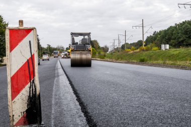 Ağır titreşimli paten sıkıştırıcılı asfalt yol silindiri bir yol inşaatındaki yolda yeni bir sıcak asfalta bastırıyor. Asfalt kaldırımda ağır titreşimli silindir çalışıyor. Onarılıyor.
