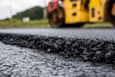 Ağır titreşimli paten sıkıştırıcılı asfalt yol silindiri bir yol inşaatındaki yolda yeni bir sıcak asfalta bastırıyor. Asfalt kaldırımda ağır titreşimli silindir çalışıyor. Onarılıyor.