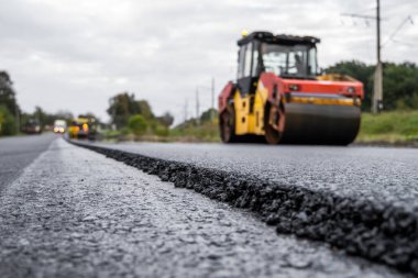 Ağır titreşimli paten sıkıştırıcılı asfalt yol silindiri bir yol inşaatındaki yolda yeni bir sıcak asfalta bastırıyor. Asfalt kaldırımda ağır titreşimli silindir çalışıyor. Onarılıyor.