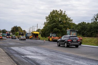 KYIV, UKRAINE - 25 Eylül 2020: İki ağır asfalt yol silindiri ve ağır titreşimli paten sıkıştırıcısı bir cadde üzerindeki yol inşaatında yeni bir sıcak asfalta baskı yapıyor..