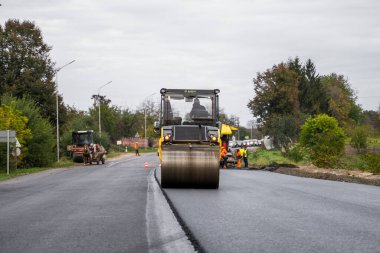 KYIV, UKRAINE - 25 Eylül 2020: İki ağır asfalt yol silindiri ve ağır titreşimli paten sıkıştırıcısı bir cadde üzerindeki yol inşaatında yeni bir sıcak asfalta baskı yapıyor..