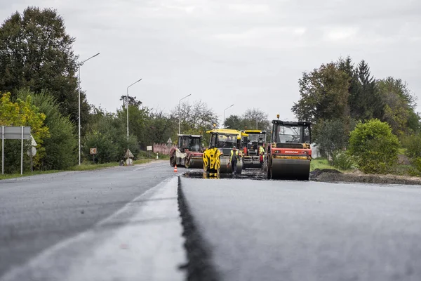 KYIV, UKRAINE - 25 Eylül 2020: İki ağır asfalt yol silindiri ve ağır titreşimli paten sıkıştırıcısı bir cadde üzerindeki yol inşaatında yeni bir sıcak asfalta baskı yapıyor..
