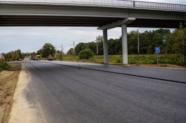 Büyük bir katman taze asfalt. Sığ bir alan derinliğinde asfalt ham madde tabakası. Patenler yeni yolda taze asfalt gibi yuvarlanıyor. Yol yapımı. Yeni bir yol inşaatı.