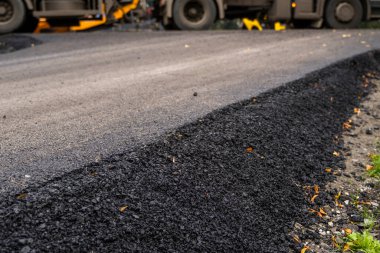 Büyük bir katman taze asfalt. Sığ bir alan derinliğinde asfalt ham madde tabakası. Patenler yeni yolda taze asfalt gibi yuvarlanıyor. Yol yapımı. Yeni bir yol inşaatı.