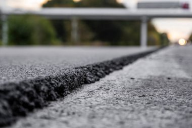 Büyük bir katman taze asfalt. Sığ bir alan derinliğinde asfalt ham madde tabakası. Patenler yeni yolda taze asfalt gibi yuvarlanıyor. Yol yapımı. Yeni bir yol inşaatı.