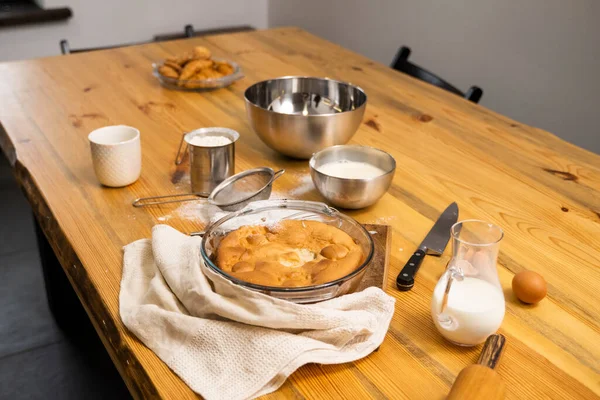 Lekkere appeltaart op een eikenhouten tafel met een ingrediënt. Een heerlijke appeltaart koken op een keuken in een loft stijl. Melk, eieren, suiker en een gebakken taart op tafel. Huiskeuken. — Stockfoto