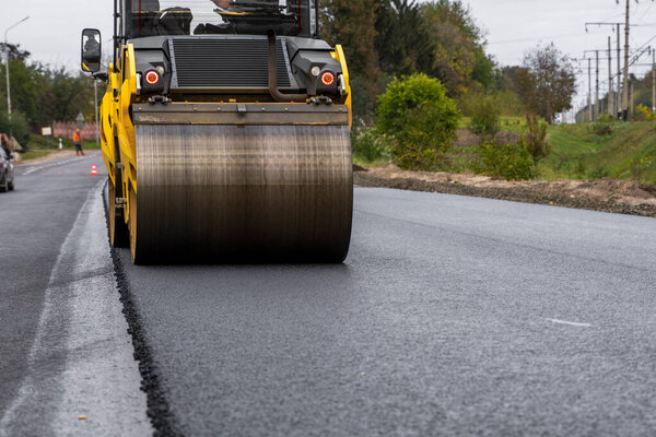 Asphalt road roller with heavy vibration roller compactor press new hot asphalt on the roadway on a road construction site. Heavy Vibration roller at asphalt pavement working. Repairing.