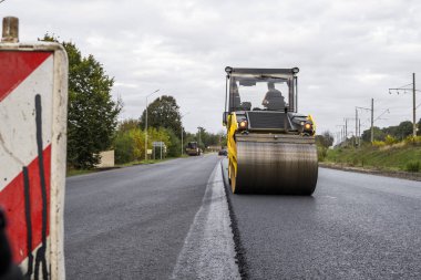 Ağır titreşimli paten sıkıştırıcılı asfalt yol silindiri bir yol inşaatındaki yolda yeni bir sıcak asfalta bastırıyor. Asfalt kaldırımda ağır titreşimli silindir çalışıyor. Onarılıyor.