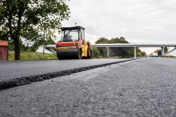 Asphalt road roller with heavy vibration roller compactor press new hot asphalt on the roadway on a road construction site. Heavy Vibration roller at asphalt pavement working. Repairing.