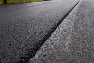 Büyük bir katman taze asfalt. Sığ bir alan derinliğinde asfalt ham madde tabakası. Patenler yeni yolda taze asfalt gibi yuvarlanıyor. Yol yapımı. Yeni bir yol inşaatı.
