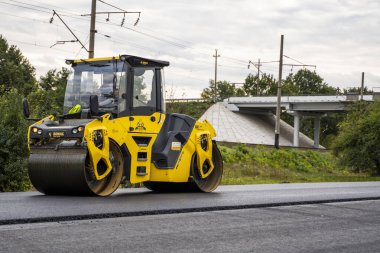 KYIV, UKRAINE - 25 Eylül 2020: Ağır sarı asfalt yol silindirli ağır titreşimli paten sıkıştırıcı bir caddedeki yol inşaatında yeni bir sıcak asfalta basıyor.