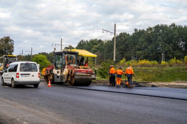KYIV, UKRAINE - 25 Eylül 2020: Ağır sarı asfalt yol silindirli ağır titreşimli paten sıkıştırıcı bir caddedeki yol inşaatında yeni bir sıcak asfalta basıyor.