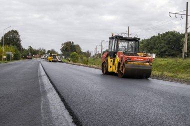 KYIV, UKRAINE - 25 Eylül 2020: İki ağır asfalt yol silindiri ve ağır titreşimli paten sıkıştırıcısı bir cadde üzerindeki yol inşaatında yeni bir sıcak asfalta baskı yapıyor..