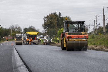 KYIV, UKRAINE - 25 Eylül 2020: İki ağır asfalt yol silindiri ve ağır titreşimli paten sıkıştırıcısı bir cadde üzerindeki yol inşaatında yeni bir sıcak asfalta baskı yapıyor..