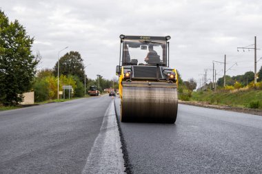 KYIV, UKRAINE - 25 Eylül 2020: İki ağır asfalt yol silindiri ve ağır titreşimli paten sıkıştırıcısı bir cadde üzerindeki yol inşaatında yeni bir sıcak asfalta baskı yapıyor..