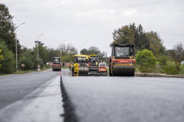 KYIV, UKRAINE - 25 Eylül 2020: İki ağır asfalt yol silindiri ve ağır titreşimli paten sıkıştırıcısı bir cadde üzerindeki yol inşaatında yeni bir sıcak asfalta baskı yapıyor..