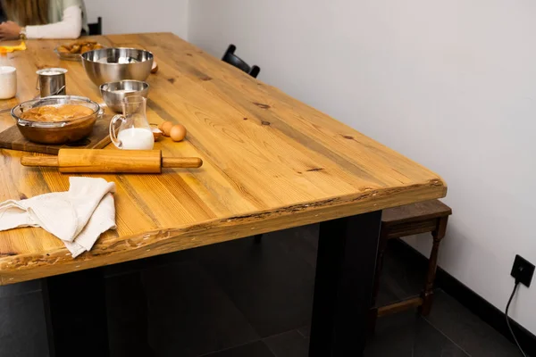 Tasty apple pie on a oaken wood table with a ingredients. Cooking a delicious apple pie on a kitchen in a loft style. Milk, eggs, sugar and a baked pie on a table. Home kitchen. — Stock Photo, Image