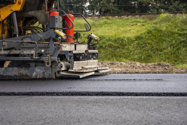 Endüstriyel asfalt kaldırım makinesi yol inşaatının üzerine taze asfalt seriyor..