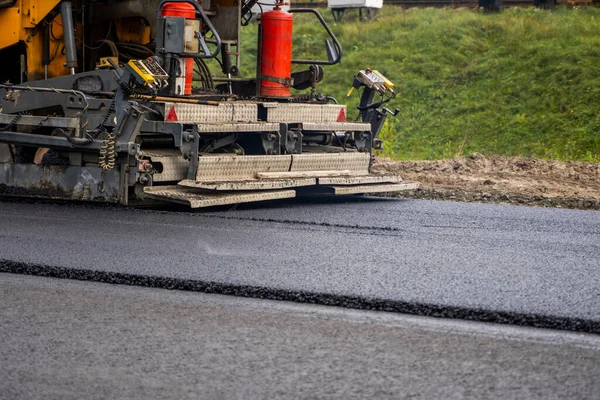 Industriell asfaltläggare maskin som lägger färsk asfalt på väg byggarbetsplats. — Stockfoto